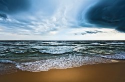 Photo of surf at beach with storm clouds in the distance.